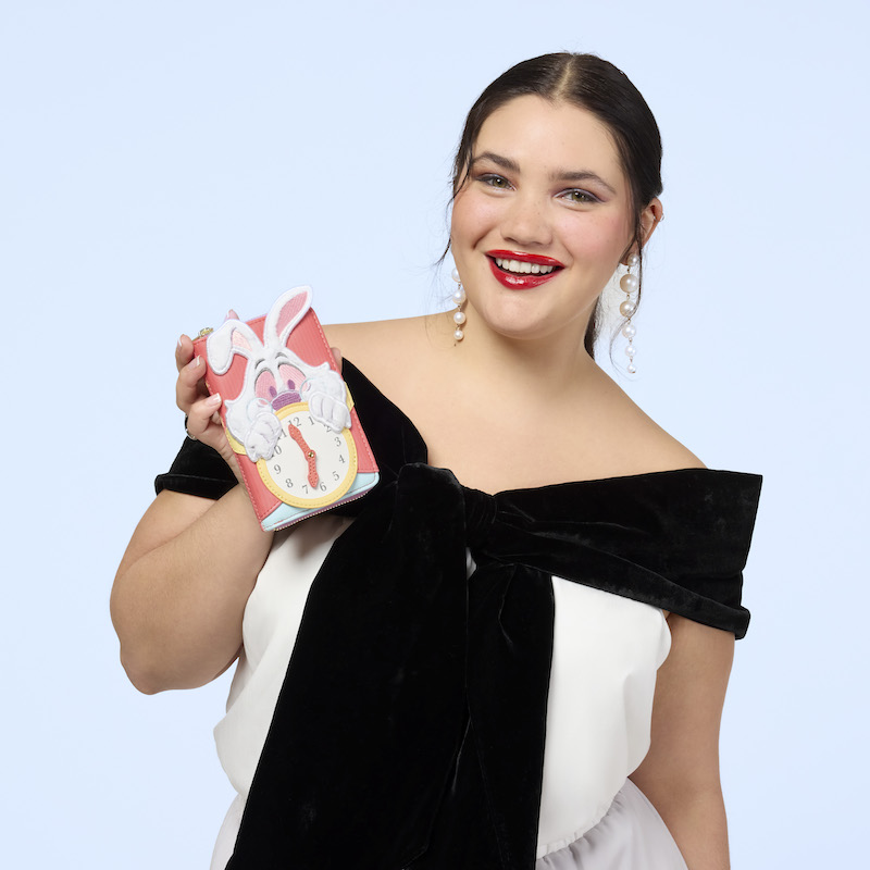 Woman wearing a black-and-white off-the-shoulder top, holding the Loungefly Alice in Wonderland White Rabbit Zip Around Wallet in one hand. 